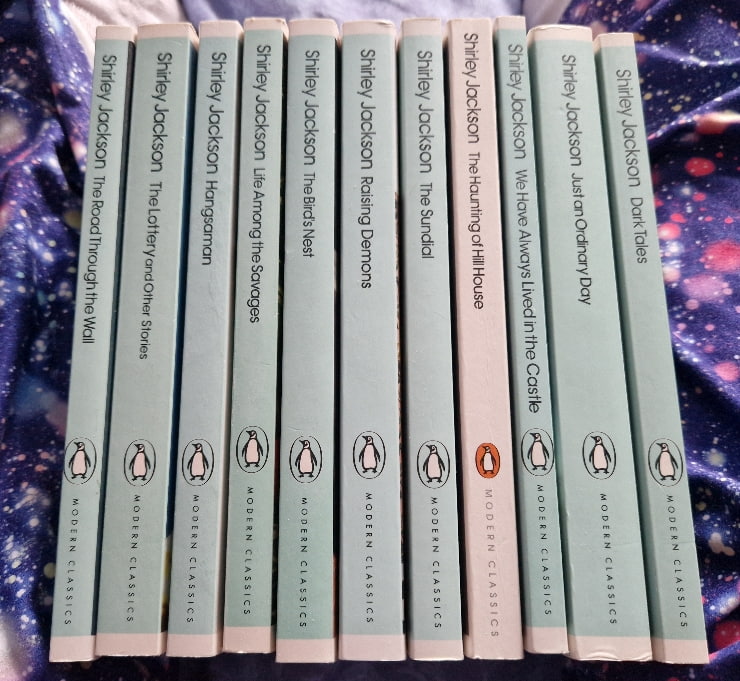 Spines of Shirley Jackson books. One, The Haunting of Hill House, is white and has an orange Penguin logo, while the others are all teal